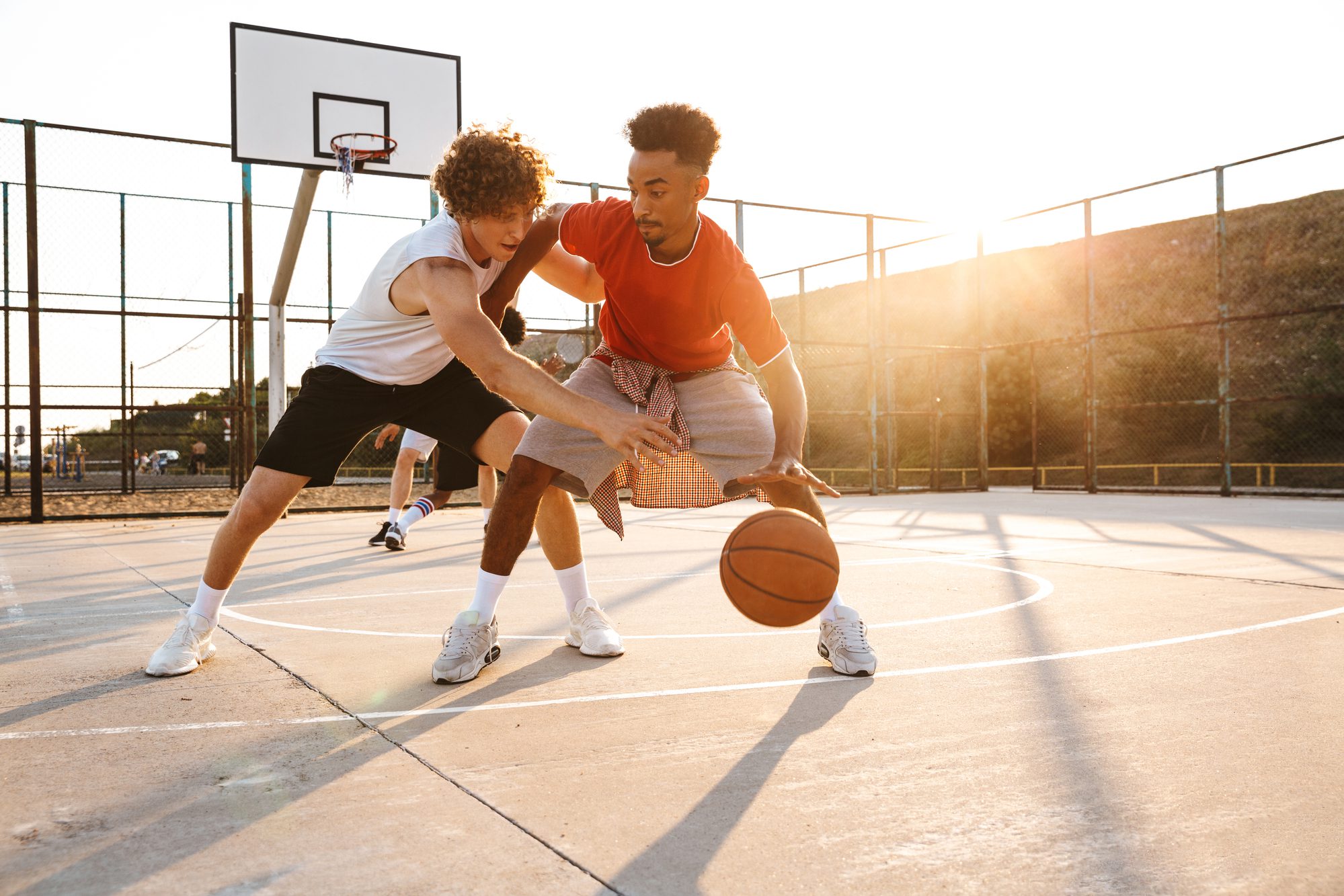 two men playing basketball on an outdoor court